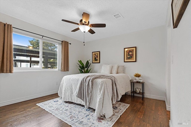 bedroom with ceiling fan, a textured ceiling, visible vents, wood finished floors, and baseboards
