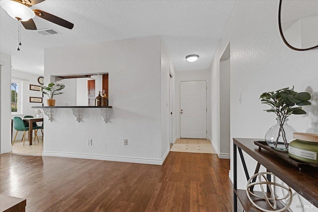 interior space featuring a textured ceiling, baseboards, visible vents, and wood finished floors