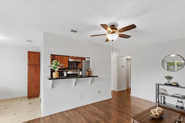 living area featuring a textured ceiling, ceiling fan, wood finished floors, and visible vents