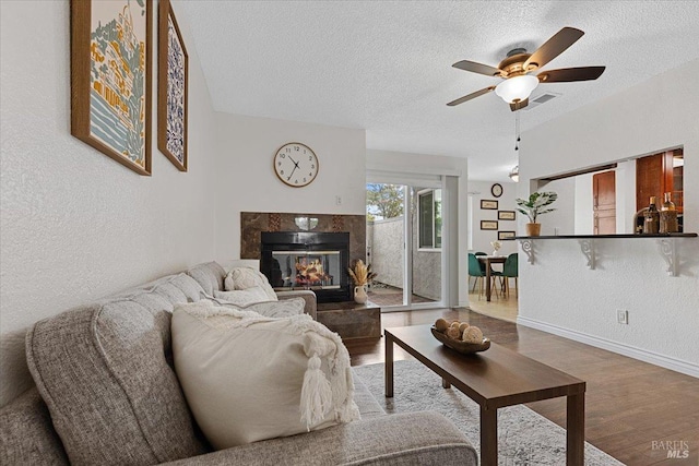 living area with a textured ceiling, ceiling fan, wood finished floors, and a fireplace