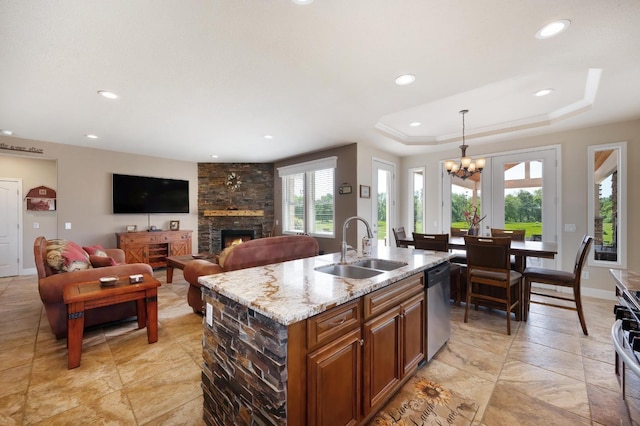 kitchen with stainless steel appliances, a sink, a chandelier, light stone counters, and a fireplace