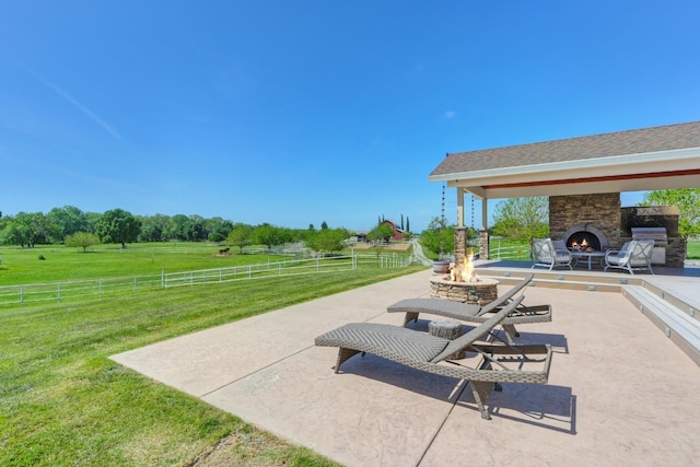 view of patio featuring a rural view, an outdoor stone fireplace, a fire pit, and fence