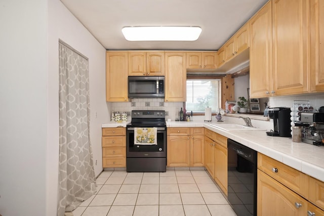 kitchen with light brown cabinetry, a sink, stainless steel microwave, black dishwasher, and electric stove