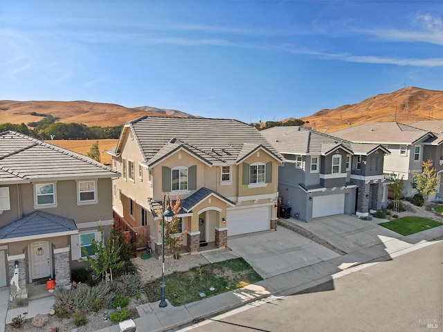 traditional home with concrete driveway, a tiled roof, an attached garage, a mountain view, and stucco siding