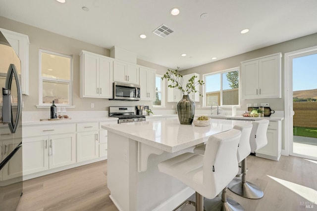 kitchen with white cabinets, appliances with stainless steel finishes, light wood-style floors, and visible vents