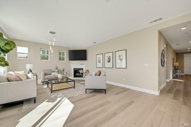 living room featuring visible vents, a glass covered fireplace, baseboards, and wood finished floors