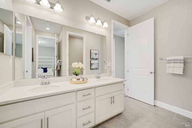 ensuite bathroom featuring baseboards, tile patterned floors, a sink, and double vanity