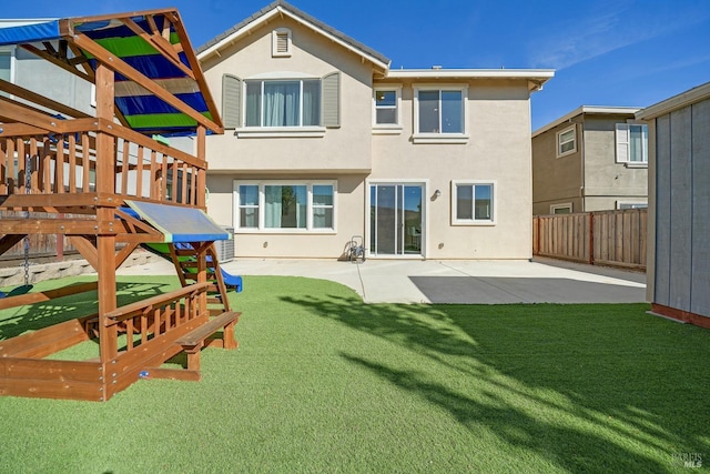 back of house with a patio area, a playground, fence, a yard, and stucco siding