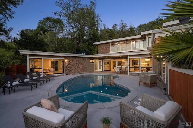 rear view of property featuring an outdoor pool, a patio area, an outdoor living space, and stone siding