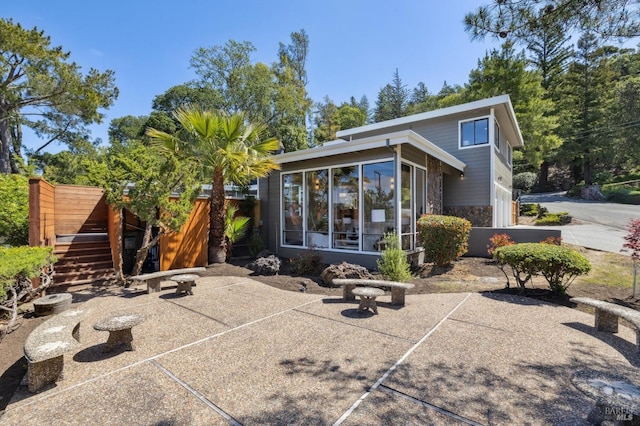 back of house featuring stone siding, stairway, a patio, and a sunroom
