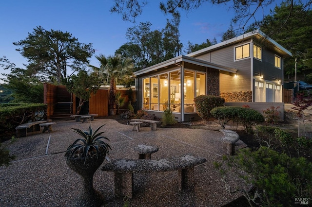 back of house with a sunroom, a patio, driveway, stone siding, and an attached garage