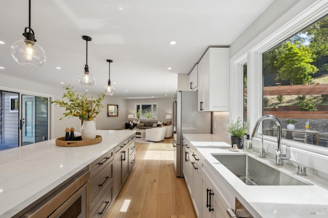 kitchen with white cabinetry, light stone countertops, open floor plan, and a sink