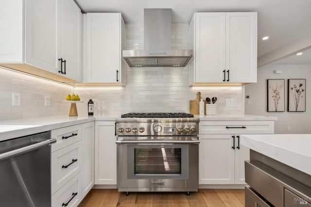 kitchen with white cabinets, appliances with stainless steel finishes, light wood-type flooring, wall chimney exhaust hood, and backsplash