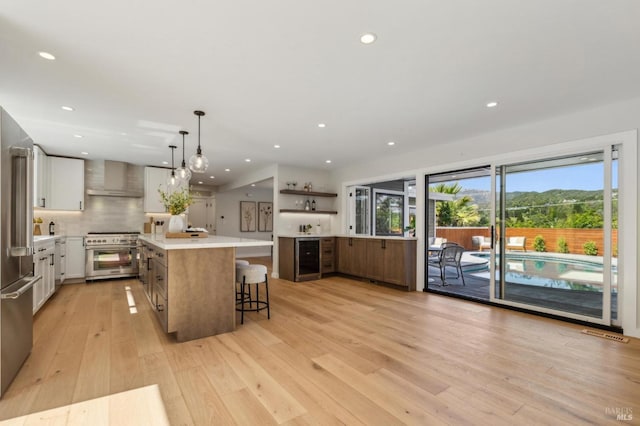 kitchen with a breakfast bar, light wood finished floors, white cabinetry, premium appliances, and wall chimney exhaust hood
