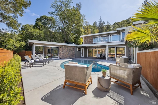 rear view of property with fence, a fenced in pool, a balcony, and a patio area