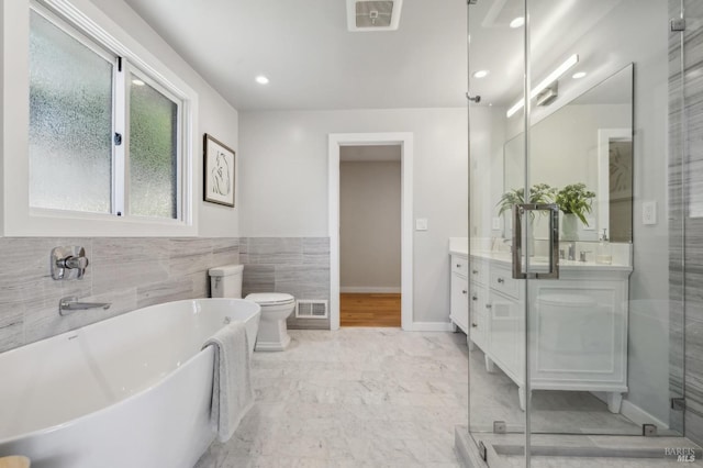 bathroom with a freestanding tub, tile walls, visible vents, and double vanity