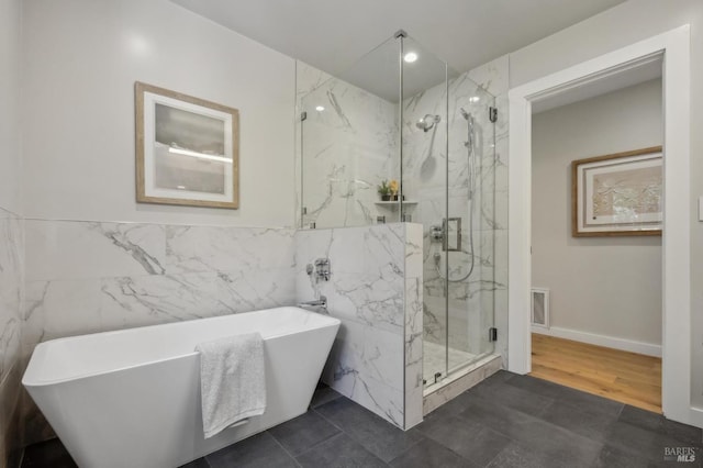 bathroom with a marble finish shower, tile walls, a freestanding bath, and visible vents