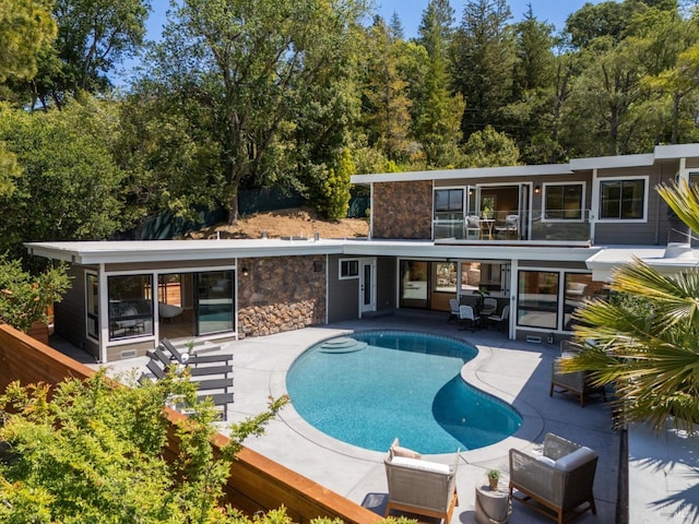 rear view of property featuring a patio area, an outdoor pool, and stone siding
