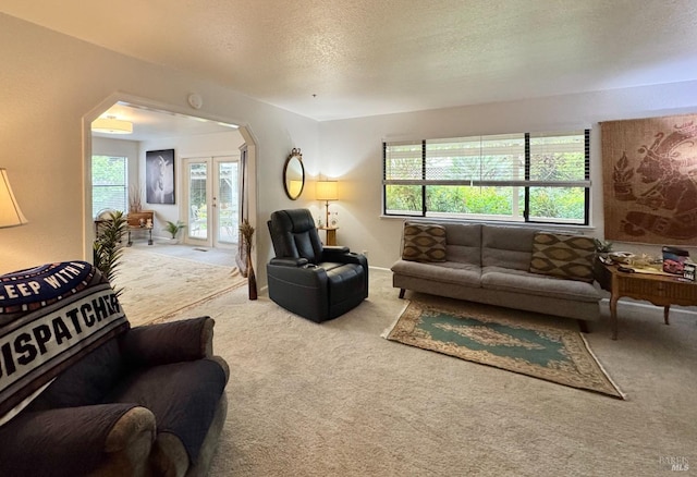 carpeted living area featuring arched walkways, a textured ceiling, and a wealth of natural light