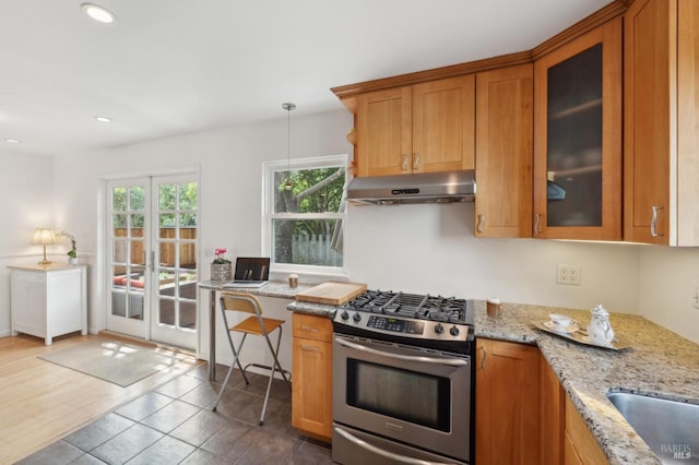 kitchen with light stone countertops, brown cabinetry, under cabinet range hood, and stainless steel gas range