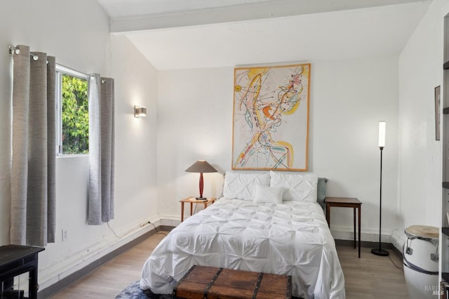 bedroom featuring baseboards, wood finished floors, and beamed ceiling
