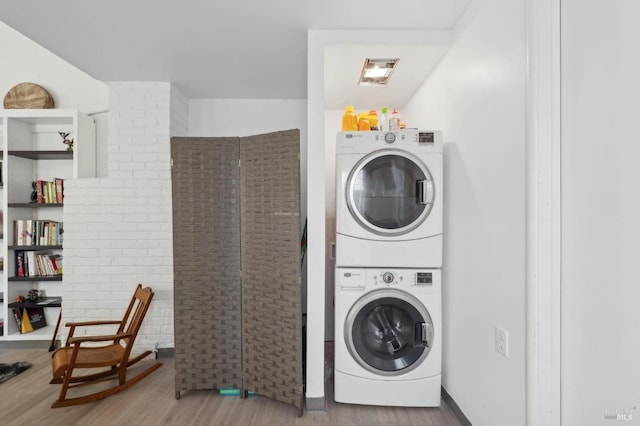 clothes washing area featuring wood finished floors, stacked washer / dryer, and laundry area