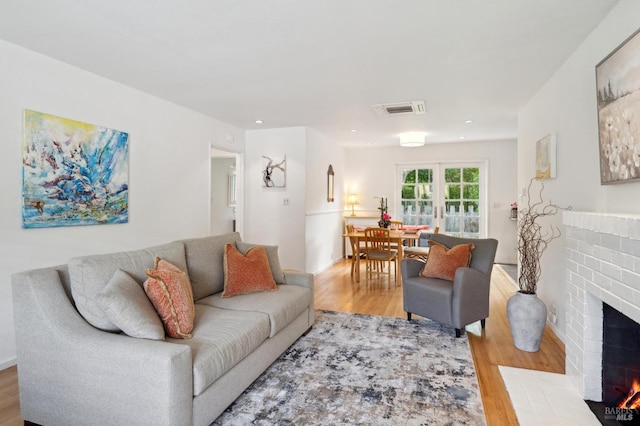 living room with a brick fireplace, wood finished floors, visible vents, and recessed lighting