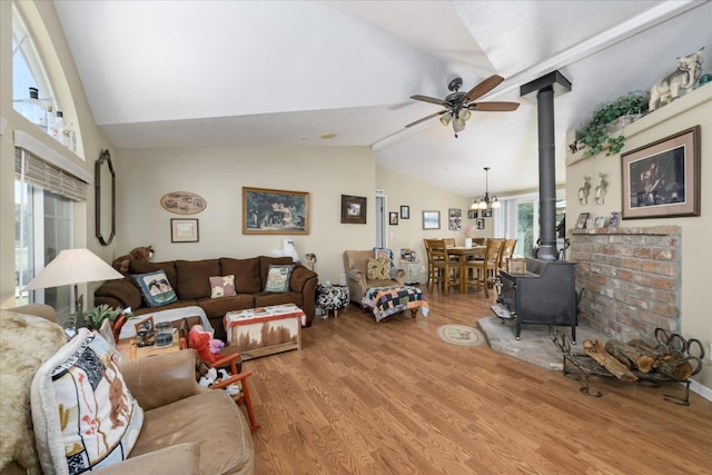 living room featuring lofted ceiling, wood finished floors, a wood stove, and ceiling fan with notable chandelier