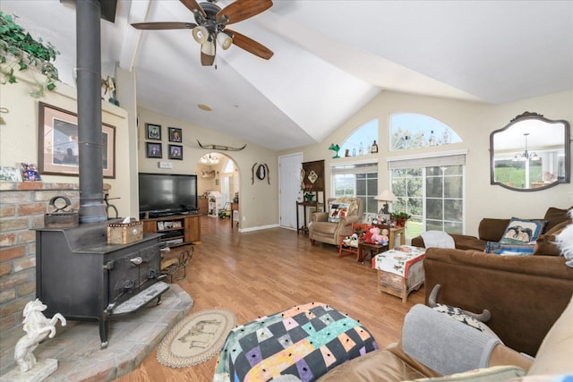 living area with light wood finished floors, vaulted ceiling, a wood stove, a ceiling fan, and baseboards
