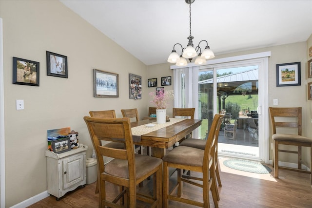 dining area with wood finished floors, lofted ceiling, baseboards, and a notable chandelier