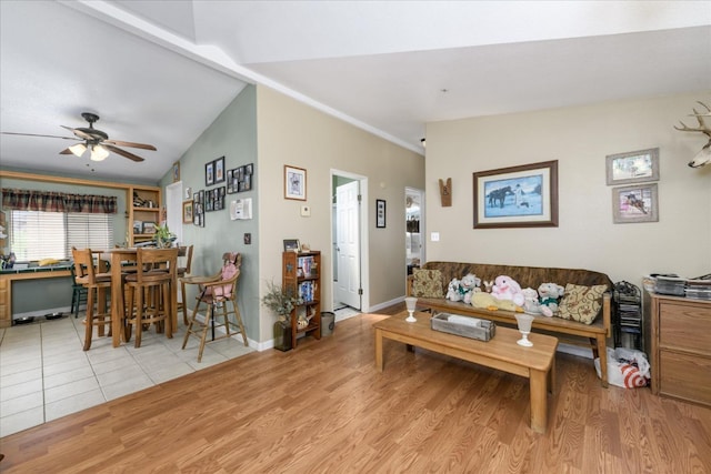 living room featuring light wood-type flooring, a ceiling fan, baseboards, and vaulted ceiling