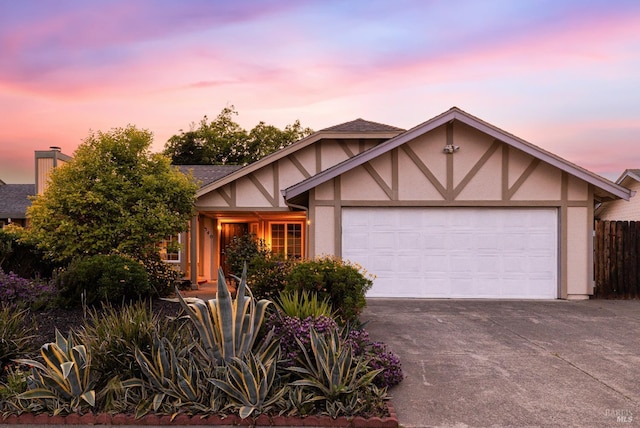 english style home featuring fence, a shingled roof, stucco siding, driveway, and a garage