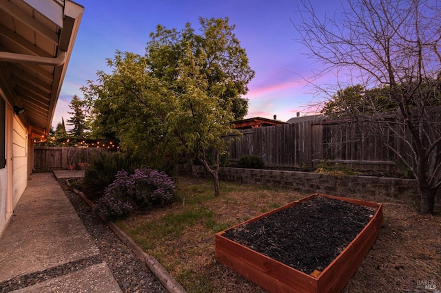yard at dusk featuring a fenced backyard and a vegetable garden