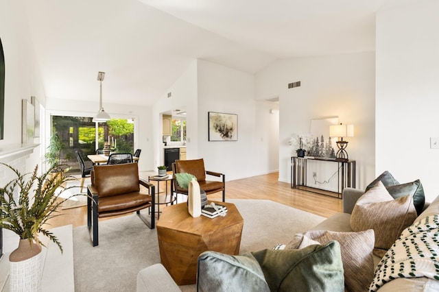 living area featuring light wood-style floors, vaulted ceiling, and visible vents