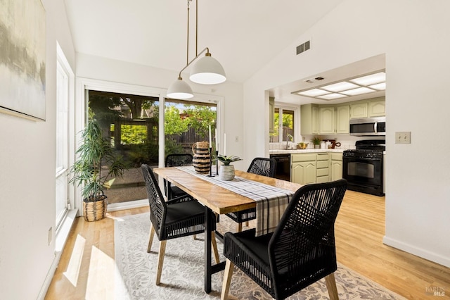 dining space featuring baseboards, light wood-style flooring, visible vents, and high vaulted ceiling