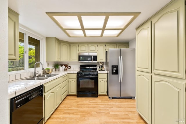 kitchen featuring light wood finished floors, a sink, tile countertops, and black appliances