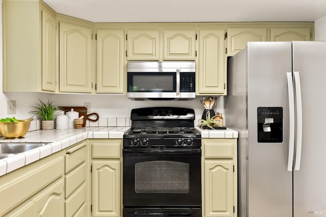 kitchen with tile countertops, cream cabinetry, and stainless steel appliances
