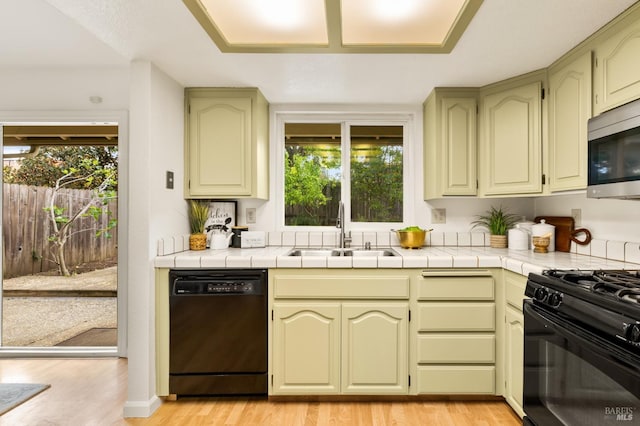kitchen featuring a sink, light wood-style floors, green cabinets, tile counters, and black appliances