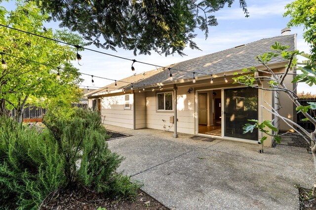 rear view of property with a patio area, a shingled roof, and fence