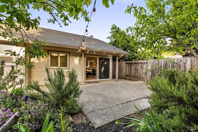back of property with fence, a patio area, and roof with shingles