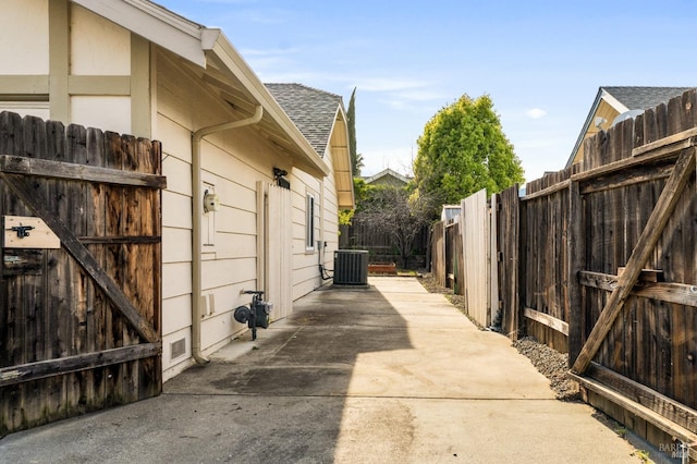 view of home's exterior featuring roof with shingles, cooling unit, driveway, fence, and a patio area