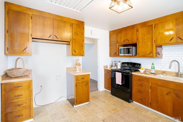 kitchen with a sink, stainless steel microwave, tasteful backsplash, black electric range oven, and brown cabinetry