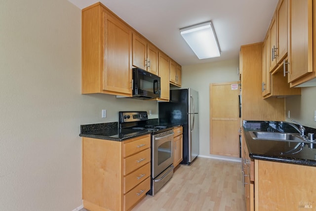 kitchen with a sink, stainless steel range with electric cooktop, black microwave, light wood finished floors, and baseboards