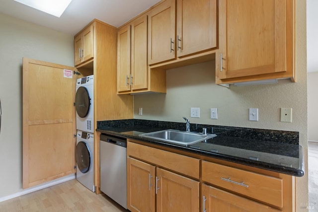kitchen featuring stainless steel dishwasher, light wood-style flooring, a sink, dark stone counters, and stacked washer / dryer