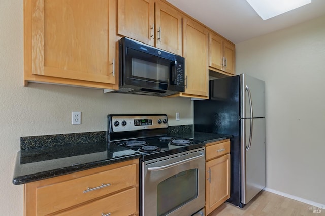 kitchen with dark stone counters, baseboards, stainless steel appliances, and light wood-style floors
