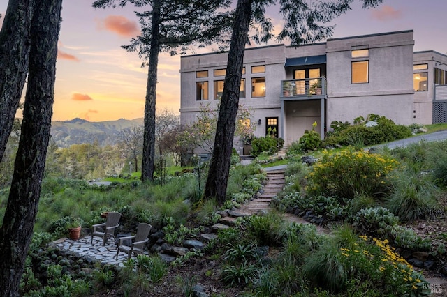 back of house at dusk featuring a balcony, stairway, stucco siding, and a mountain view