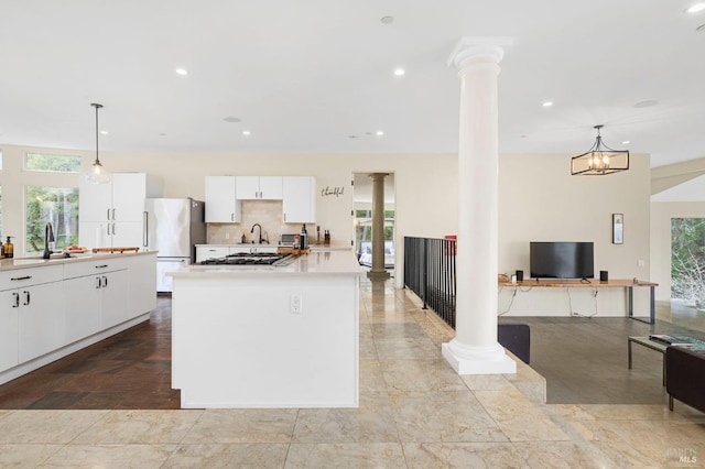 kitchen featuring decorative columns, freestanding refrigerator, a sink, a kitchen island, and white cabinetry