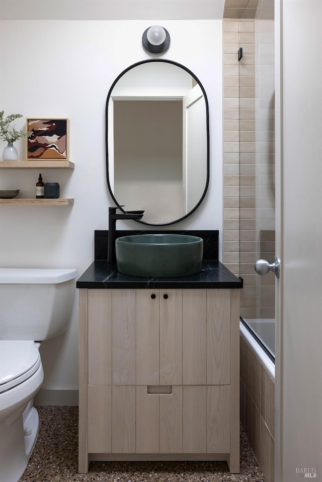 full bathroom featuring speckled floor, tiled shower / bath, toilet, vanity, and baseboards