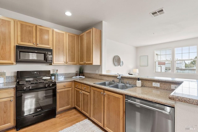 kitchen featuring visible vents, a peninsula, a sink, light wood finished floors, and black appliances
