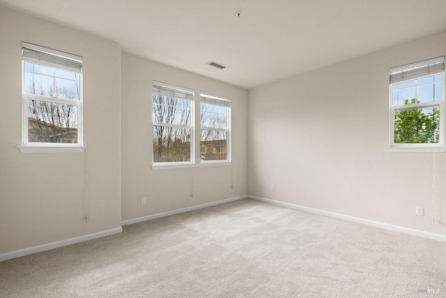 empty room with baseboards, a wealth of natural light, light colored carpet, and visible vents